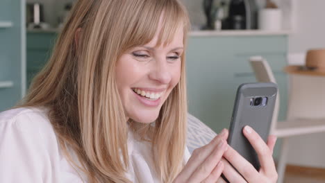 beautiful blonde woman having video chat using smartphone smiling looking surprised enjoying good news chatting to friend on mobile phone at home