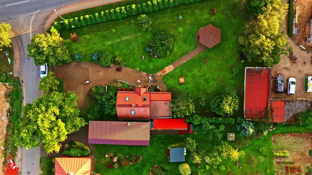 Aerial view of rural homestead with houses, trees, garden plots, and dirt roads