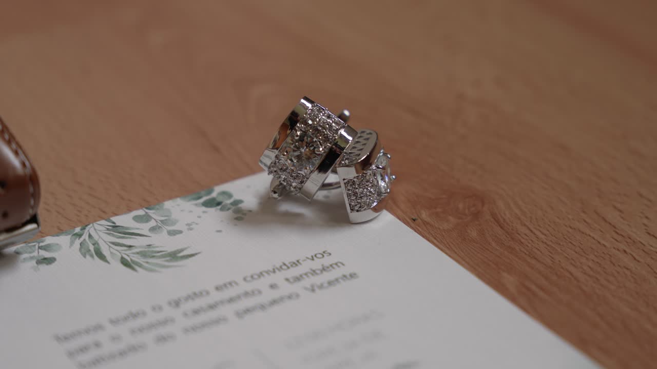 shiny rings placed on floral wedding invitation on wooden surface