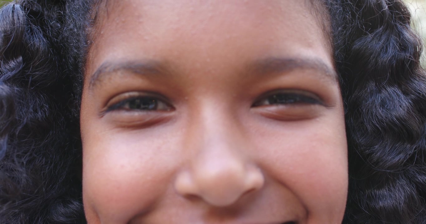 Camera pulling back, African American female youth smiling, shifting head outside, engaging viewer