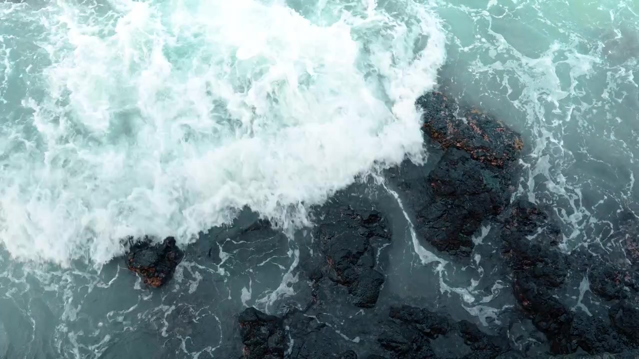 Overhead view of swirling ocean waves, Isabela Island, Galapagos. Top down perspective of white sea foam washing over dark volcanic rocks in turquoise water.