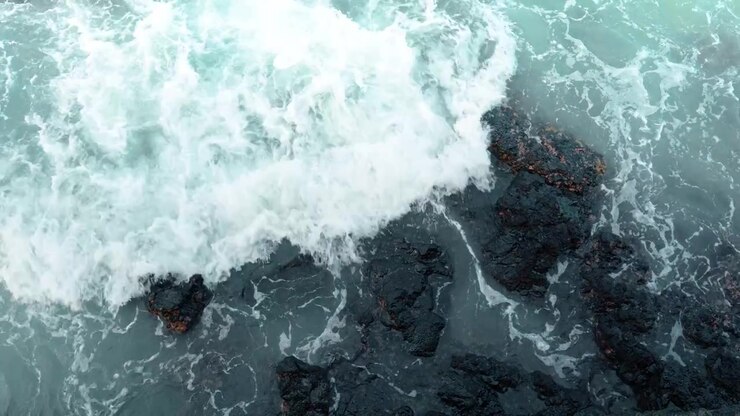 Overhead view of swirling ocean waves, Isabela Island, Galapagos. Top down perspective of white sea foam washing over dark volcanic rocks in turquoise water.