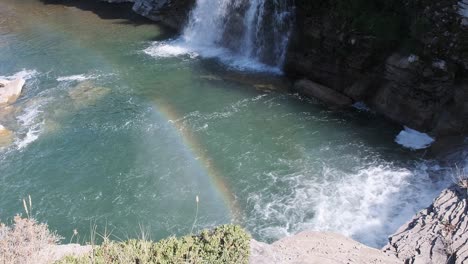 Bright-colourful-rainbow-forms-in-river-mist-of-raging-white-waterfall