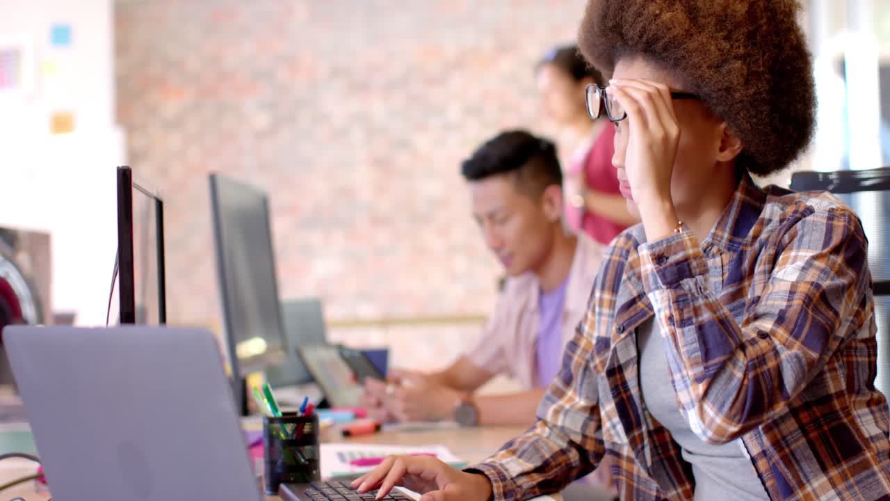 Thoughtful biracial creative businesswoman working at computer in casual office, slow motion