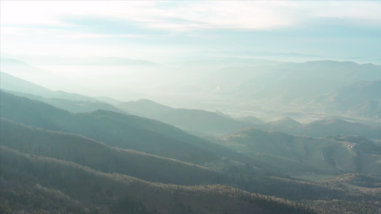 Aerial flyover of a forest-covered mountain range in the morning with fog.