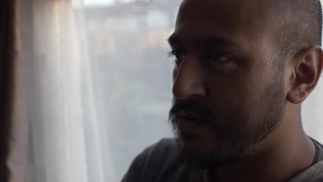 adult asian male thinking looking forward next to backlit window with white curtains