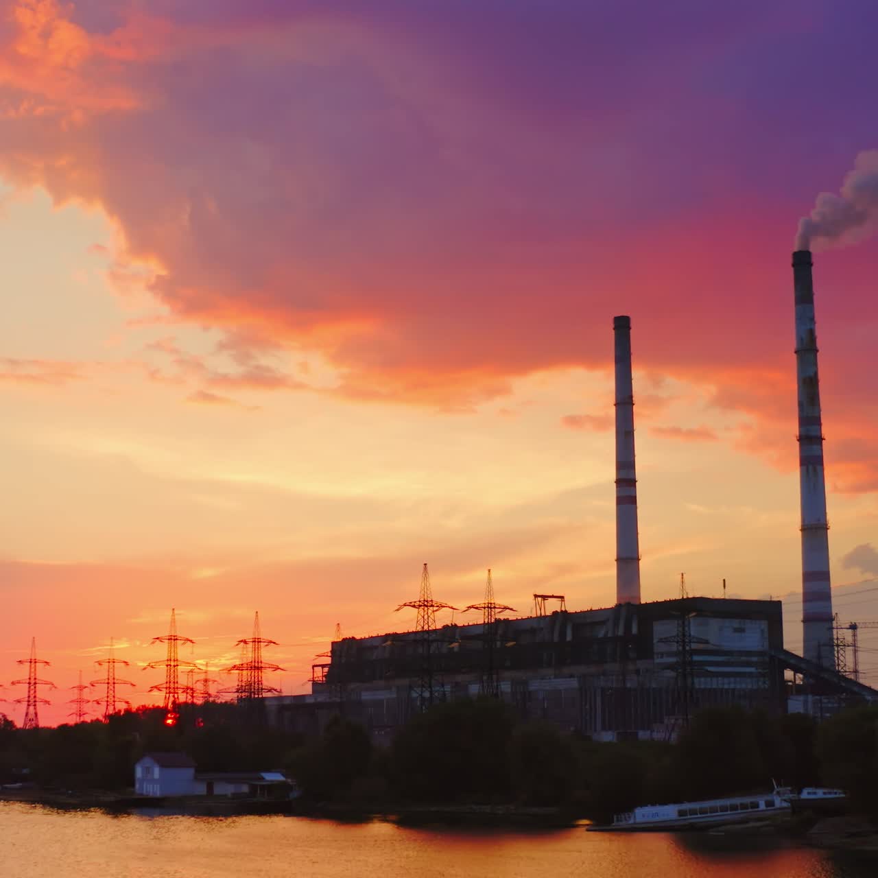 Industrial area at sunset. Factory near the river on the beautiful pink sky. Harmful manufacture with smoke goes from industrial pipe in the evening.