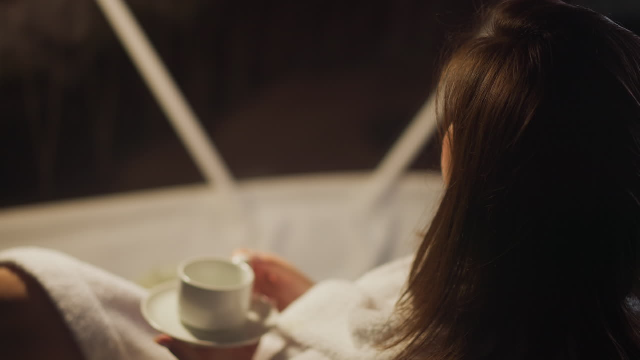 집중된 여성은 파노라마 창문에서 자연의 야간 생활을 지켜보고 관광 호텔에서 커피를 마시고, 황혼에 혼자 휴식과 휴식을 취합니다.