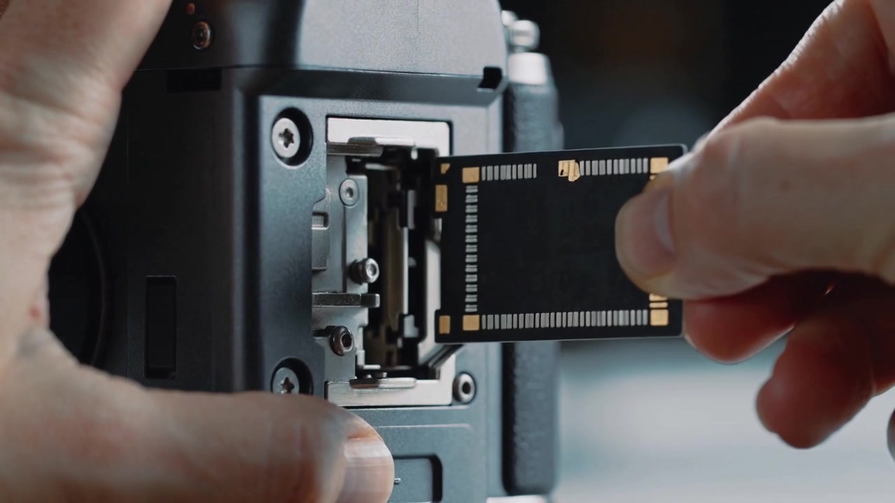 Opening card compartment, operator hands aligning and sliding SD card into camera, preparing camera
