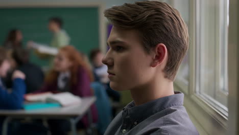 pensive male student looking out a classroom window