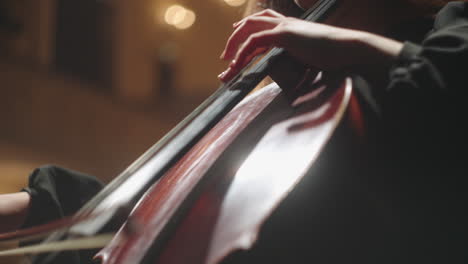 female violoncellist is playing violoncello on scene closeup of cello bow and hands of cellist