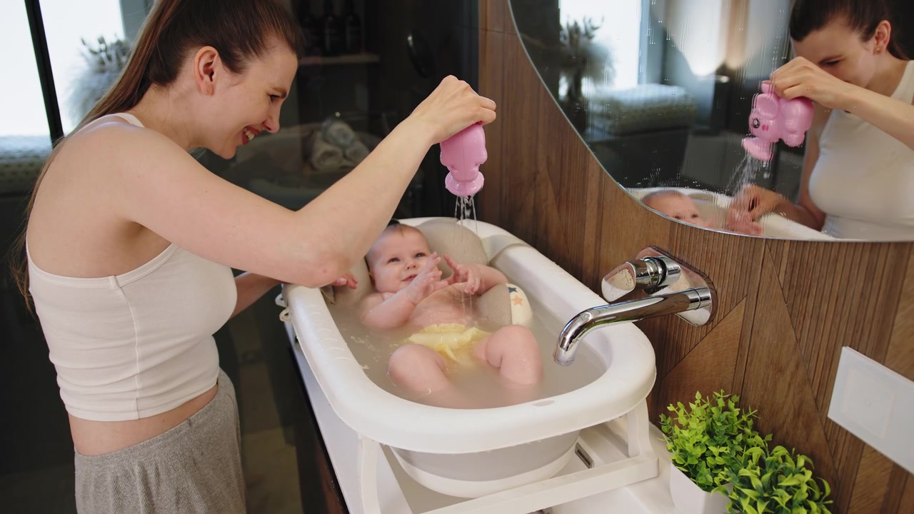 Mother washes baby in bathtub with elephant toy creating joyful moments during bath time routine a