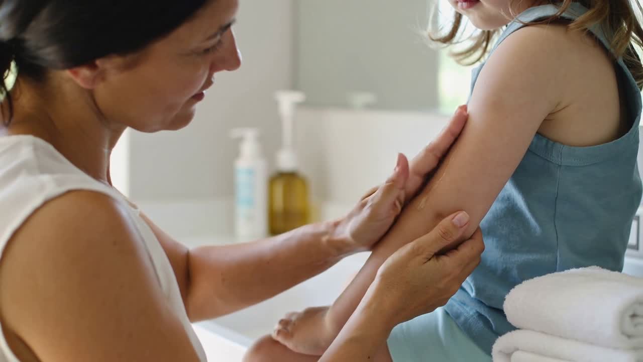 Noticing spot, caregiver in white top applying cream, treating child's arm at bathroom with towels