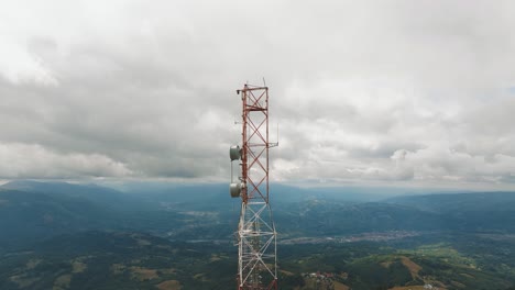 high altitude telecommunication tower holding multiple antennas, over a mountain landscape with distant small villages, aerial view