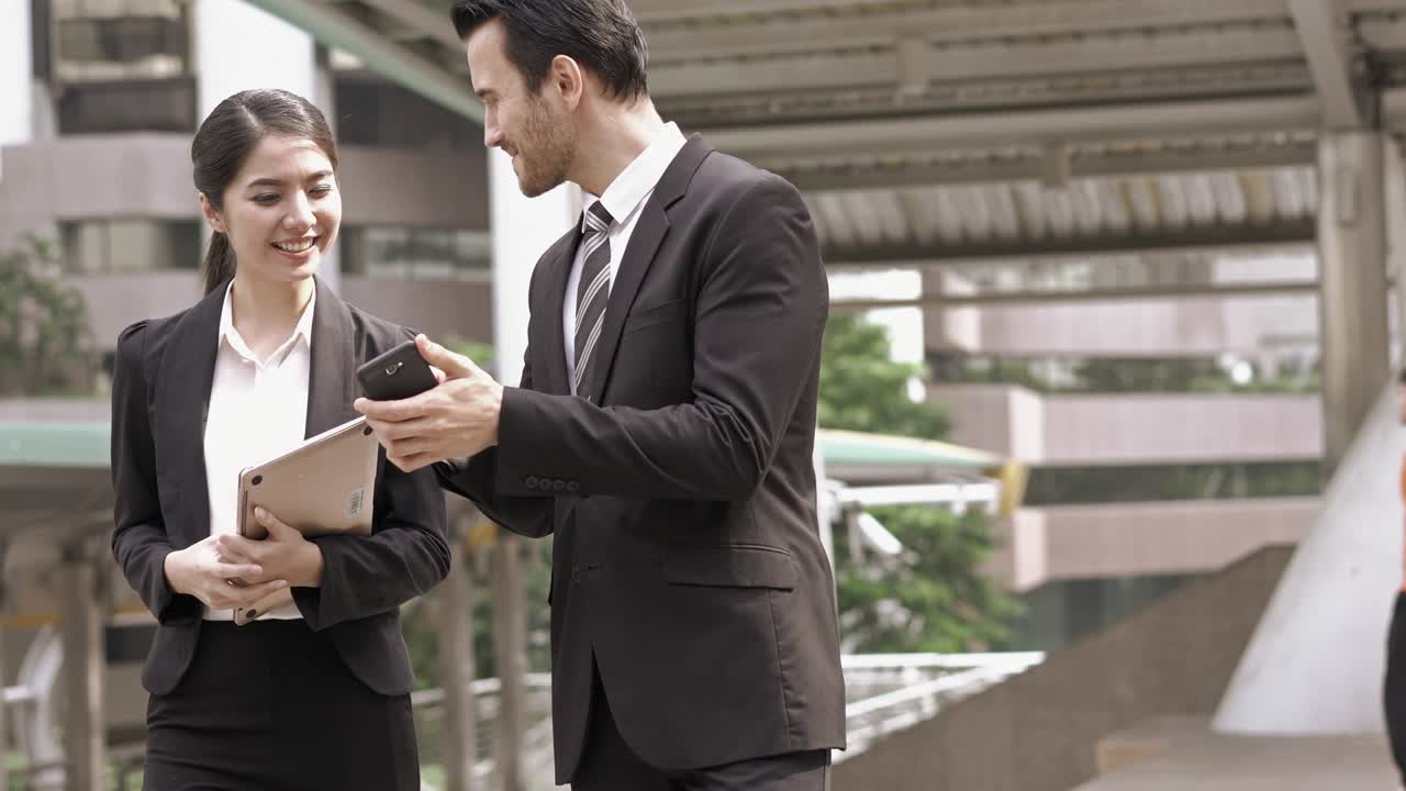 un hombre de negocios y una mujer de negocios hablando y caminando por la ciudad. una mujer con una computadora portátil en la mano.