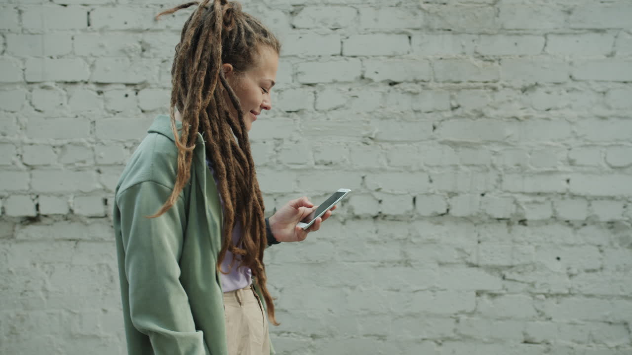 Donna con i dreadlock che usa uno smartphone all'aperto