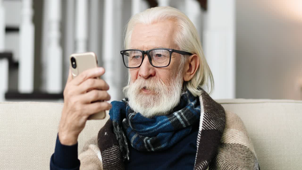 cerrar el retrato de un hombre enfermo con el pelo gris sentado en una habitación acogedora y tener una videoconferencia en el teléfono celular