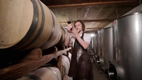 authentic shot of successful male sommelier is tasting a flavor and checking white wine quality poured in transparent glass in a wine cellar.