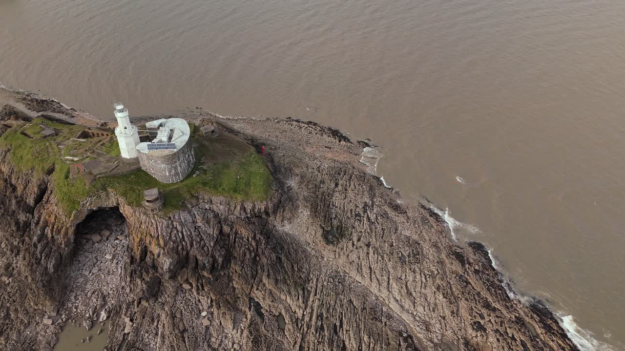 Mumbles Lighthouse standing on terrain near muddy Swansea during afternoon in England. Drone shot.