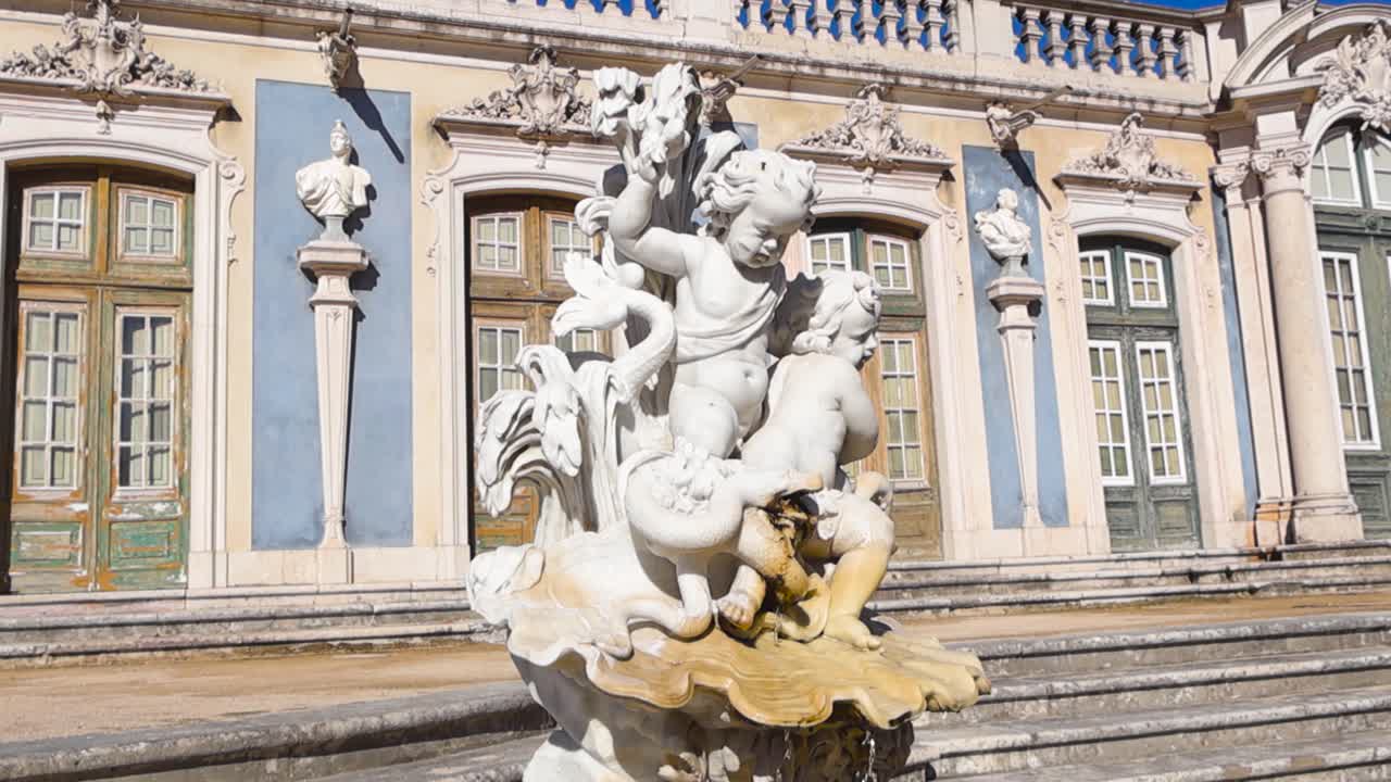 Fontana scultorea ornata nei giardini del Palazzo Nazionale di Queluz con elegante architettura barocca sotto un cielo azzurro e limpido.