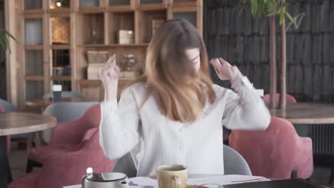 Beautiful-girl-is-sitting-in-a-cafe,-turning-the-music-on-her-phone-on-and-dancing