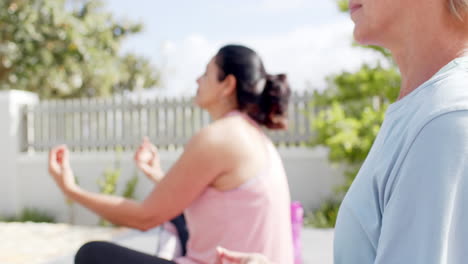 two happy diverse senior women practising yoga in sunny garden, slow motion