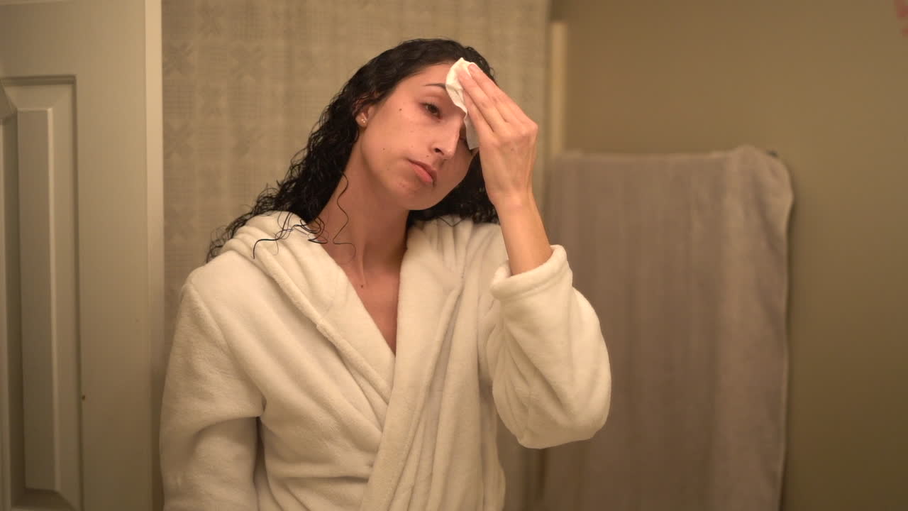 joven y atractiva mujer latina quitándose el maquillaje en su baño usando una bata de baño - aislada