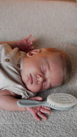 cute newborn boy lies sleeping on the sofa. lovely kid holding a hairbrush in his tiny hand. vertical video