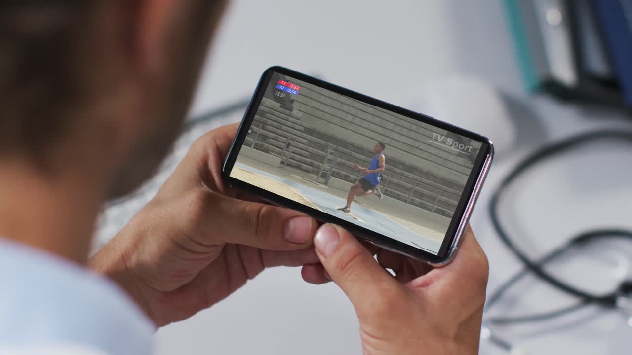compuesto de un médico masculino viendo un evento de salto de longitud de atletismo en un smartphone