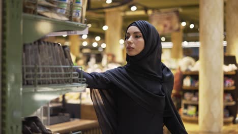 Woman-in-hijab-takes-pile-of-products-from-the-shelf-in-the-supermarket,-slow-motion