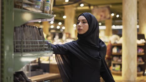 woman in hijab takes pile of products from the shelf in the supermarket, slow motion