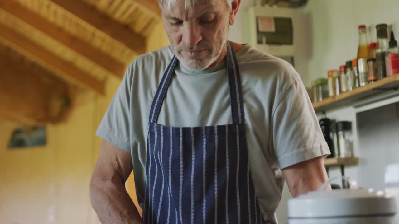 hombre caucásico mayor con delantal y cortando verduras en la cocina