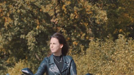 front view of beautiful woman hair waving in wind, female biker wearing leather jacket on road with autumn leaf color trees at amelisweerd forest on sunny day