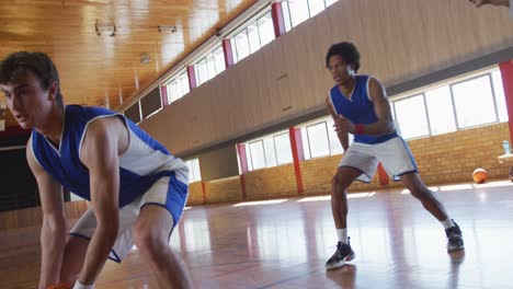 Diverse-male-basketball-team-and-coach-playing-match,-helping-each-other