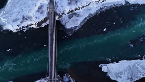 aerial top down of cars on bridge over selfoss river with ice floe in winter. snowy winter landscape in iceland.