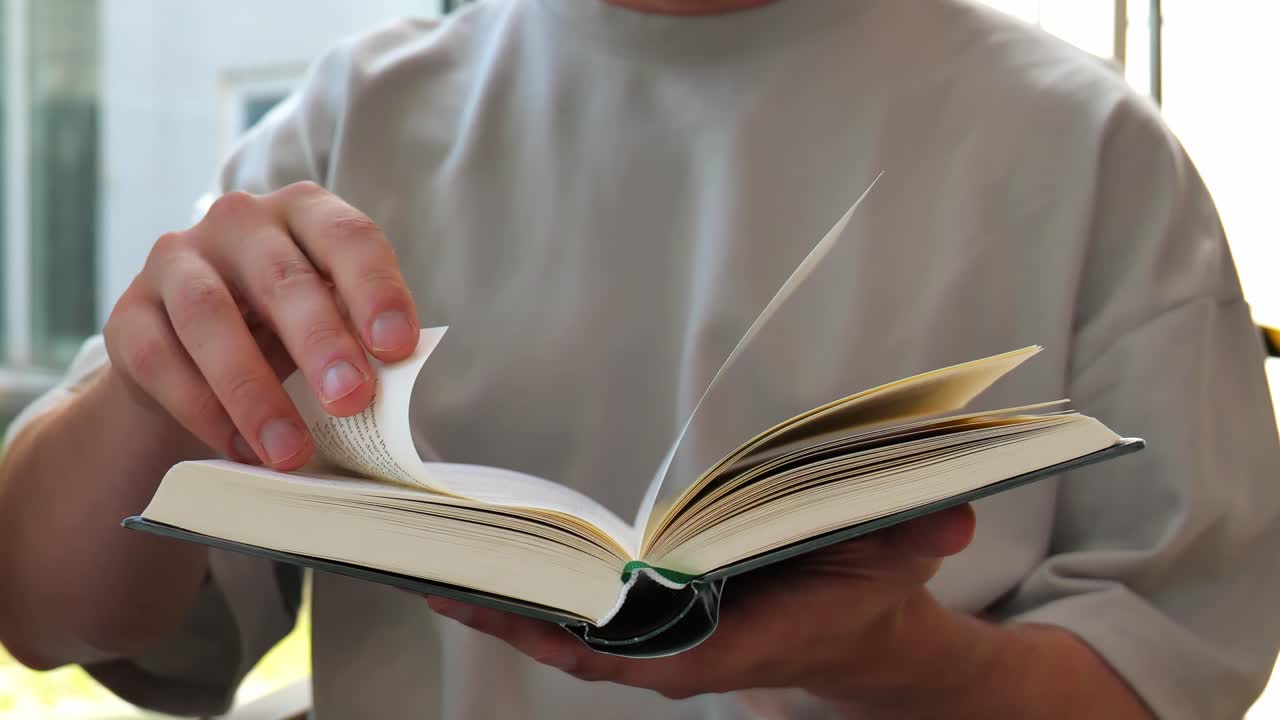 Man holding a book in his hands while reading and turning pages slowly