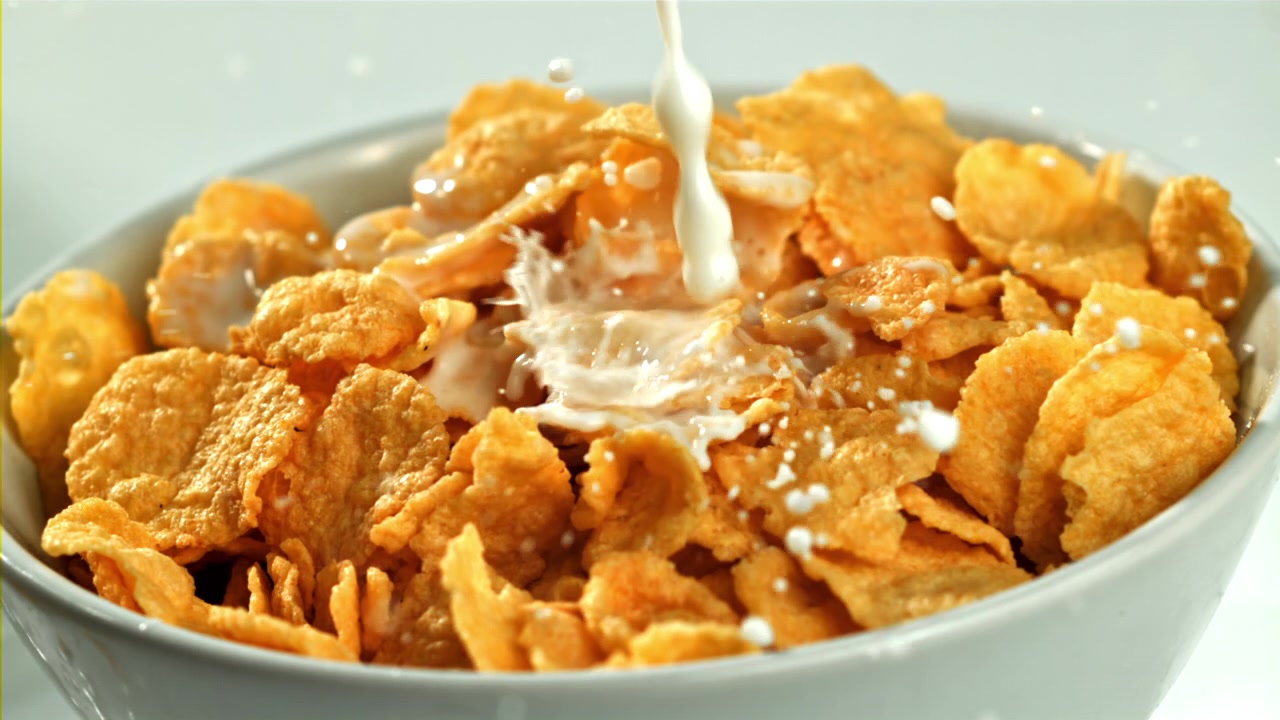 Mælk hældes i slow motion ned i en skål med gyldne cornflakes.