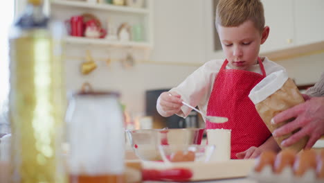 boy pours flour into a glass helps dad while baking bread