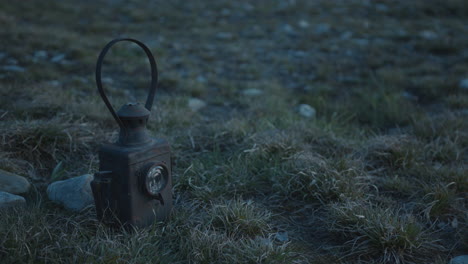 old signal lantern with warm light placed in open field at dusk