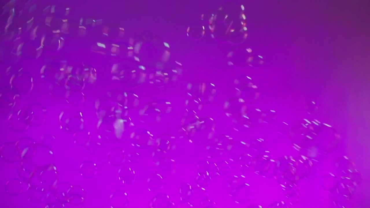 Dozens of shimmering bubbles swirl on purple background with neon reflections