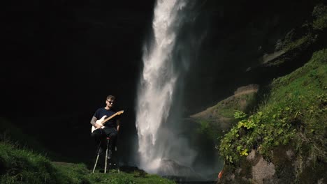 hombre tocando la guitarra frente a una hermosa cascada en islandia-14