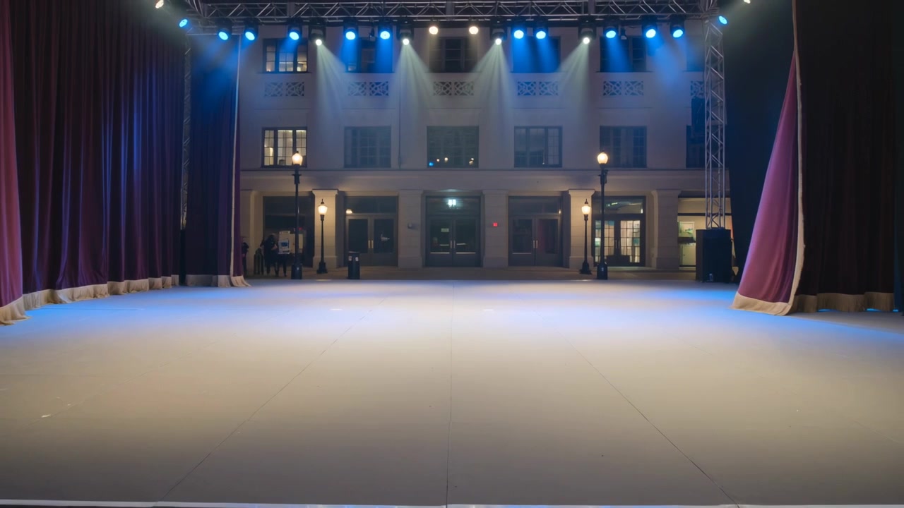 Tecnici di scena che tirano e aprono tende bordeaux sul palco, rivelando una facciata, preparando lo spettacolo.