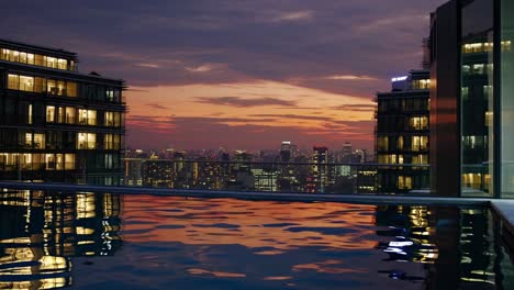 warm sunset colors reflecting in rooftop infinity pool water overlooking illuminated modern city skyline at dusk, creating serene and luxurious atmosphere