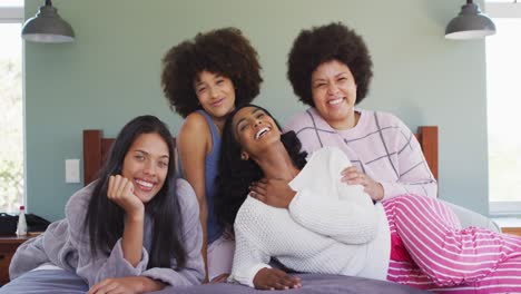 Portrait-of-happy-diverse-female-friends-lying-on-bed-and-smiling-in-bedroom