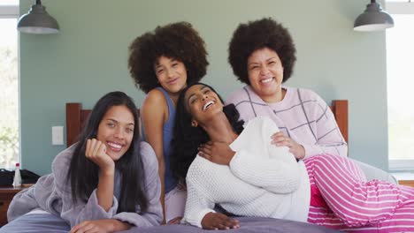 portrait of happy diverse female friends lying on bed and smiling in bedroom