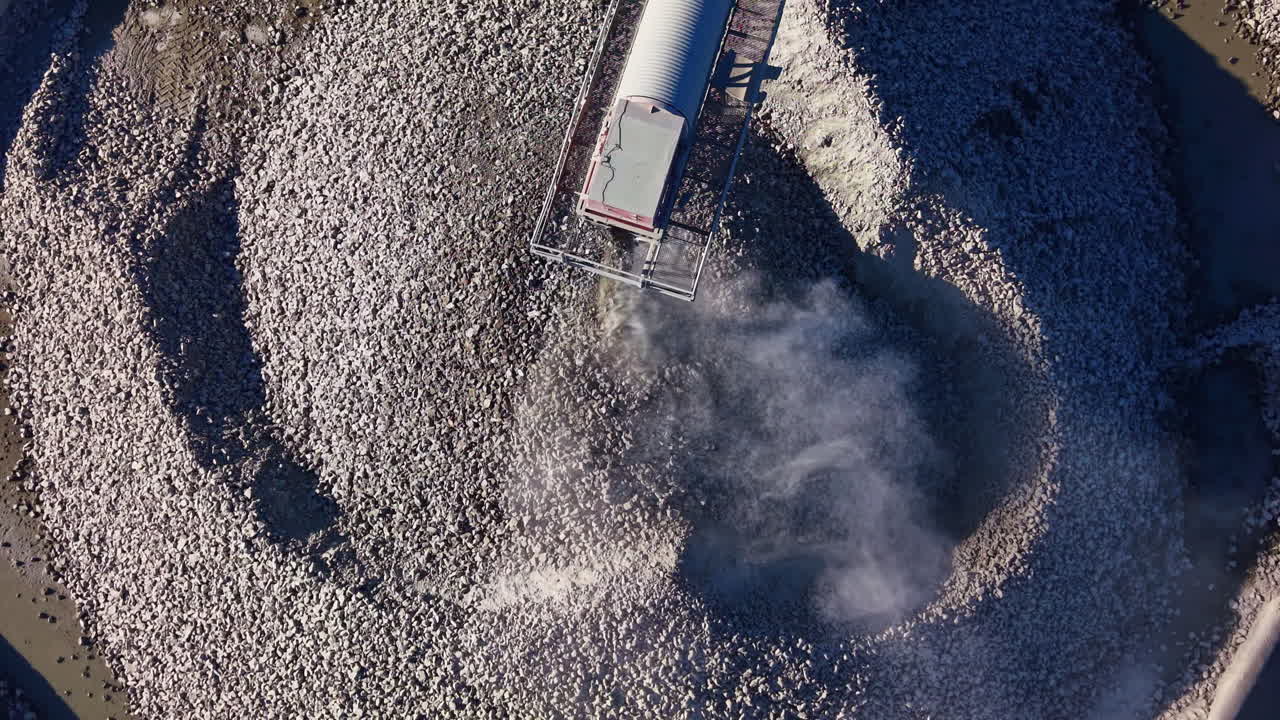 Large machinery spreads gravel across a rocky terrain under clear blue skies