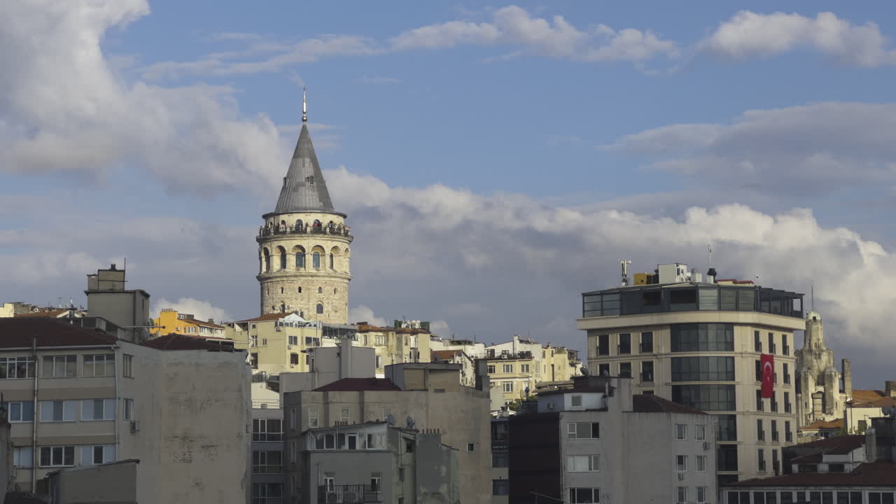torre de galata bajo un cielo despejado con los edificios circundantes visibles, enmarcada por los edificios subyacentes mientras los pájaros se elevan en el cielo