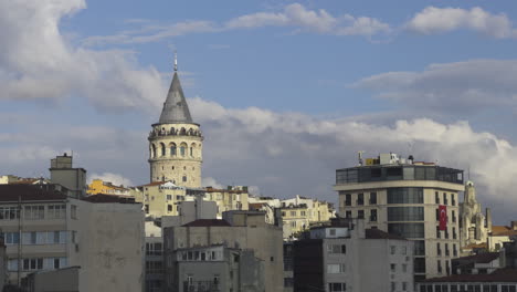 galata tower under clear sky with the surrounding buildings visible, framed by the underlying buildings as birds soar in sky