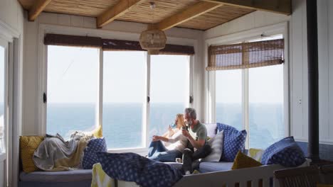 happy caucasian mature couple drinking coffee and talking in sunny living room