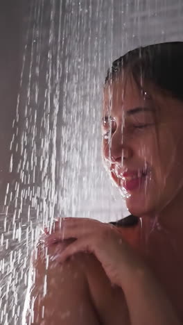 smiling woman stands in shower water closeup. happy relaxed lady spends time enjoying warm jets in home bathroom. body care procedures in washroom